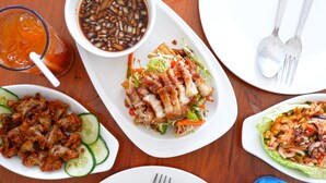 A table with various dishes including a salad with lettuce, cucumber, and red peppers, a bowl of soup, and a plate of fried chicken. - Sky Hotel Pampanga (Bacolor)