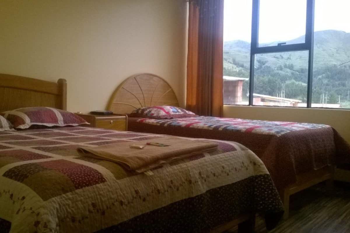 Une chambre avec deux lits, une table de chevet et une fenêtre donnant sur des collines.