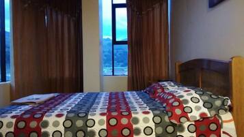 Un dormitorio con una cama cubierta por un edredón de lunares, una ventana con cortinas y vistas a un paisaje montañoso.