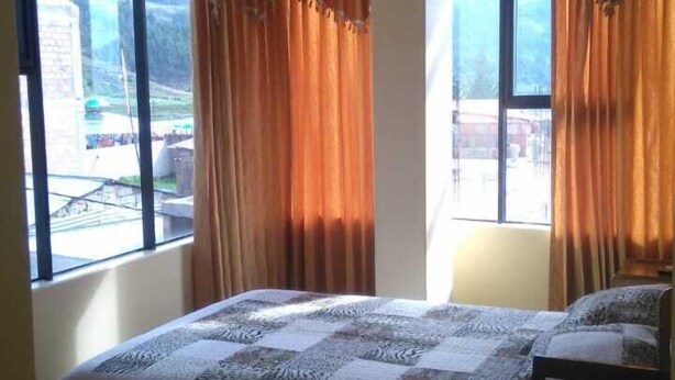 A room with a bed, a chair, and a table. There are windows with curtains.