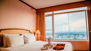 A hotel room with a large bed, a view of a cityscape through a window, and a lamp on the wall. - Yannaty Hotel Halal (Hat Yai)