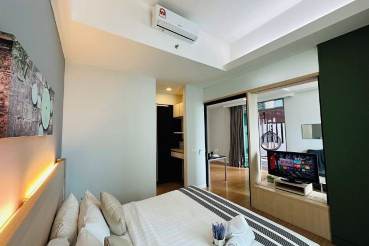 A hotel room with a bed, bedside table, TV, and an air conditioning unit.