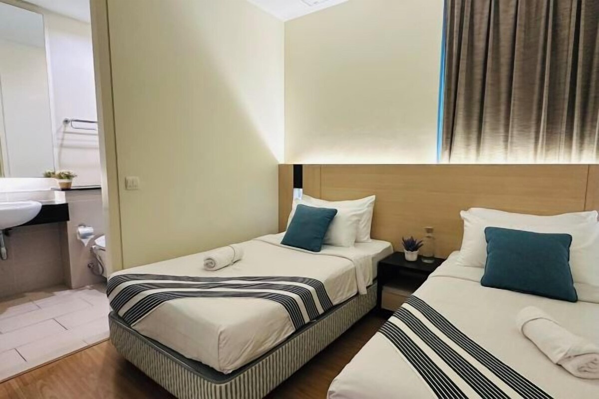 A hotel room with two beds, a nightstand, a small table, a sink, and a mirror.