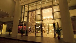 Una entrada de hotel moderna con grandes puertas de vidrio, columnas y plantas en macetas.