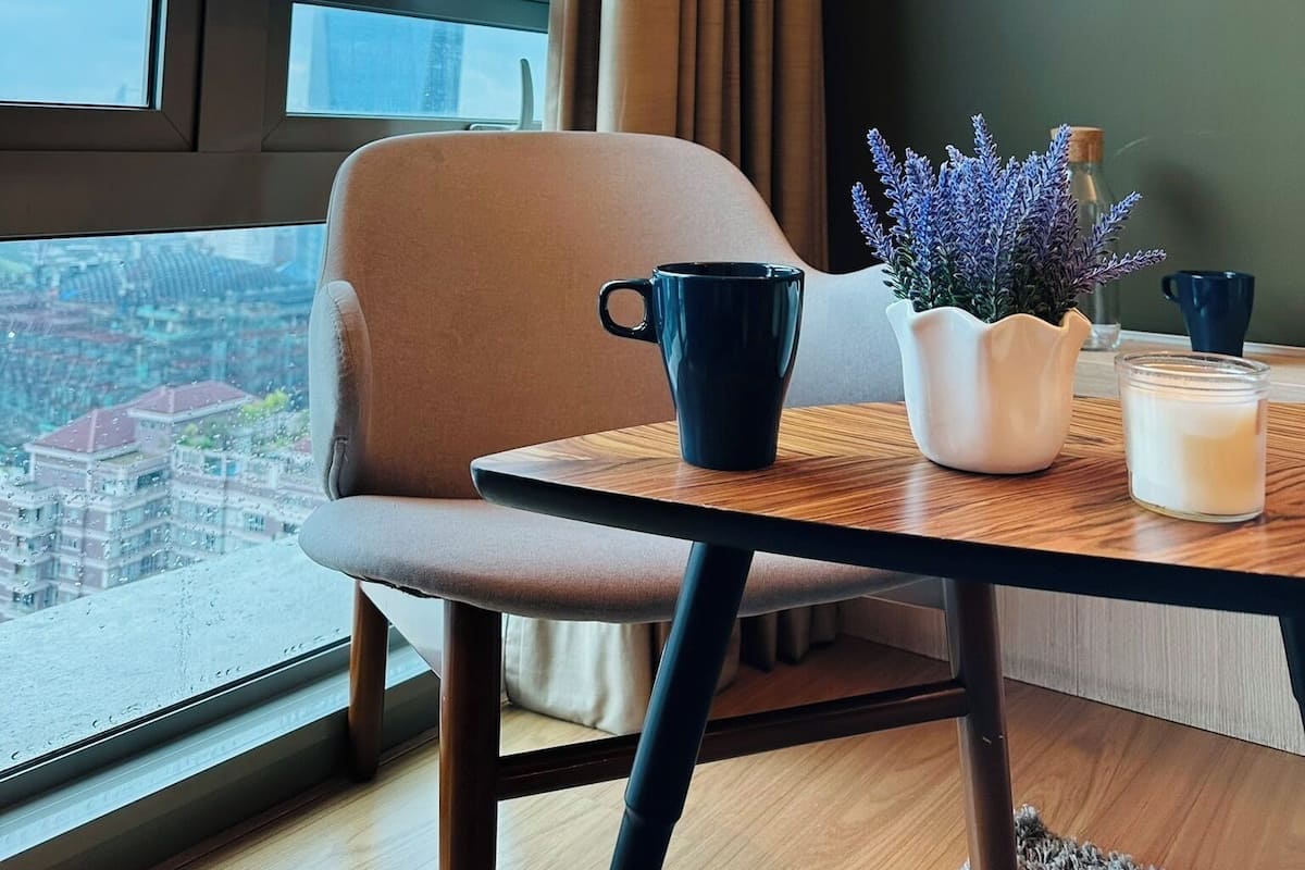 Quarto moderno com vista para um edifício alto, uma mesa com uma xícara, um vaso com flores e uma vela.