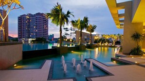 Una piscina con fuentes de agua, palmeras y edificios modernos al fondo.
