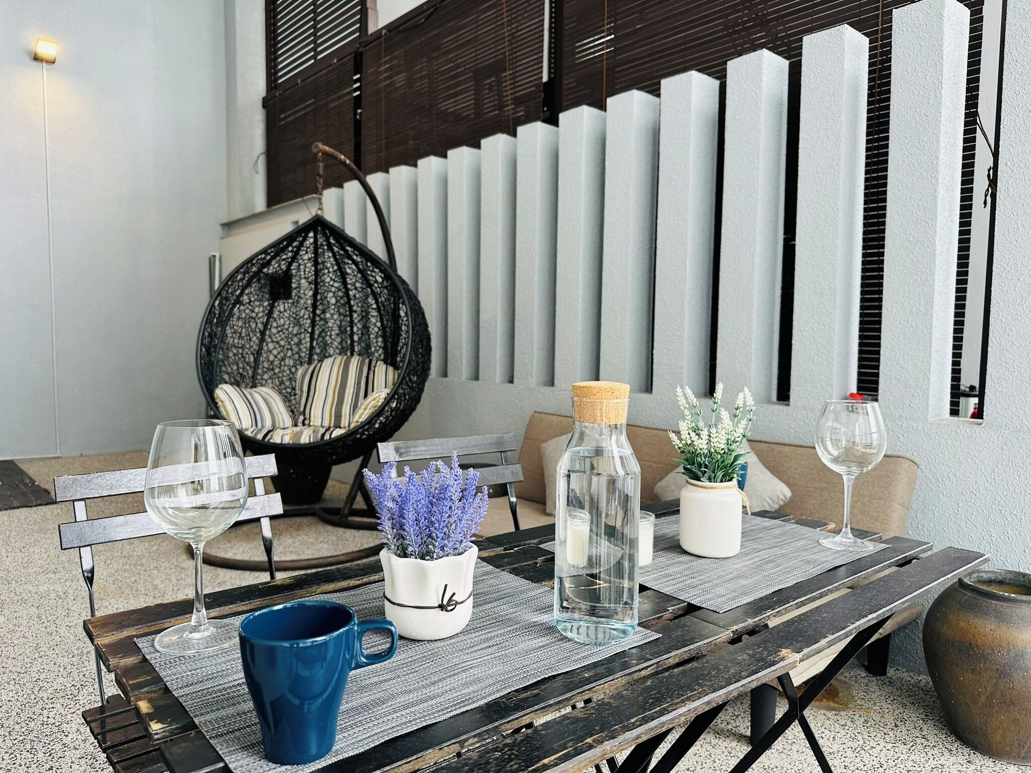 A wooden table with two wine glasses, a blue mug, and decorative items like a bottle and a potted plant.