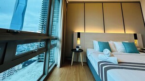 Un cuarto de hotel con un ventanal grande, una cama con almohadas, una mesita con una planta y vista a un edificio alto.