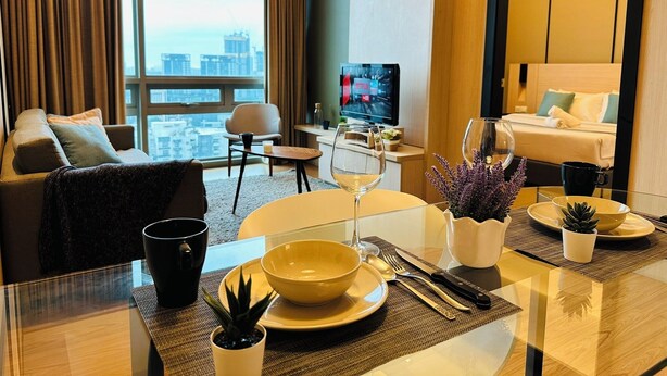 Una habitación de hotel moderna con vista a la ciudad, un comedor con mesa de vidrio y una zona de estar acogedora con sofá y sillón.