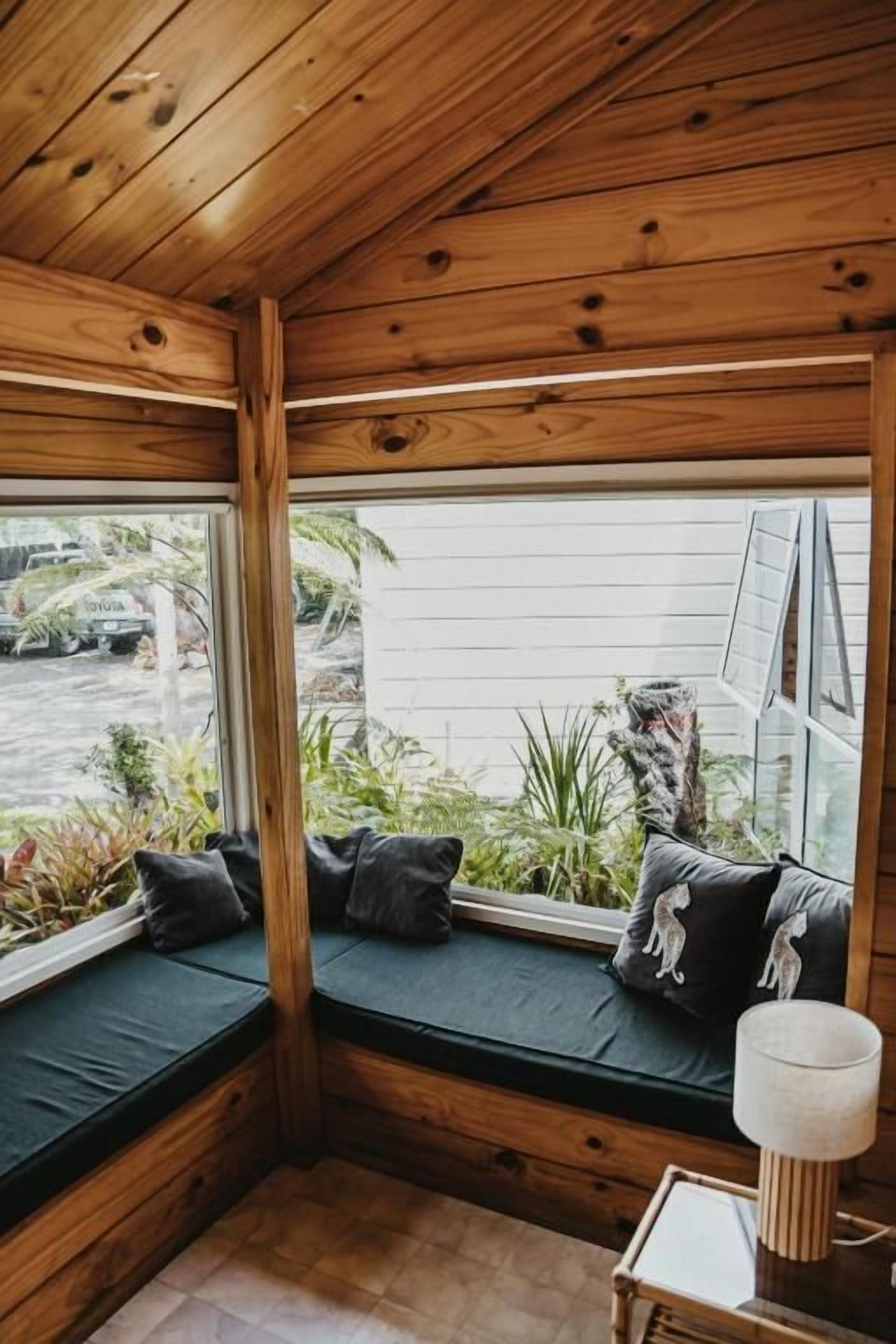 Ein Eckzimmer mit Holzboden, einer Sitzbank mit Kissen und einem kleinen Tisch mit Lampe.