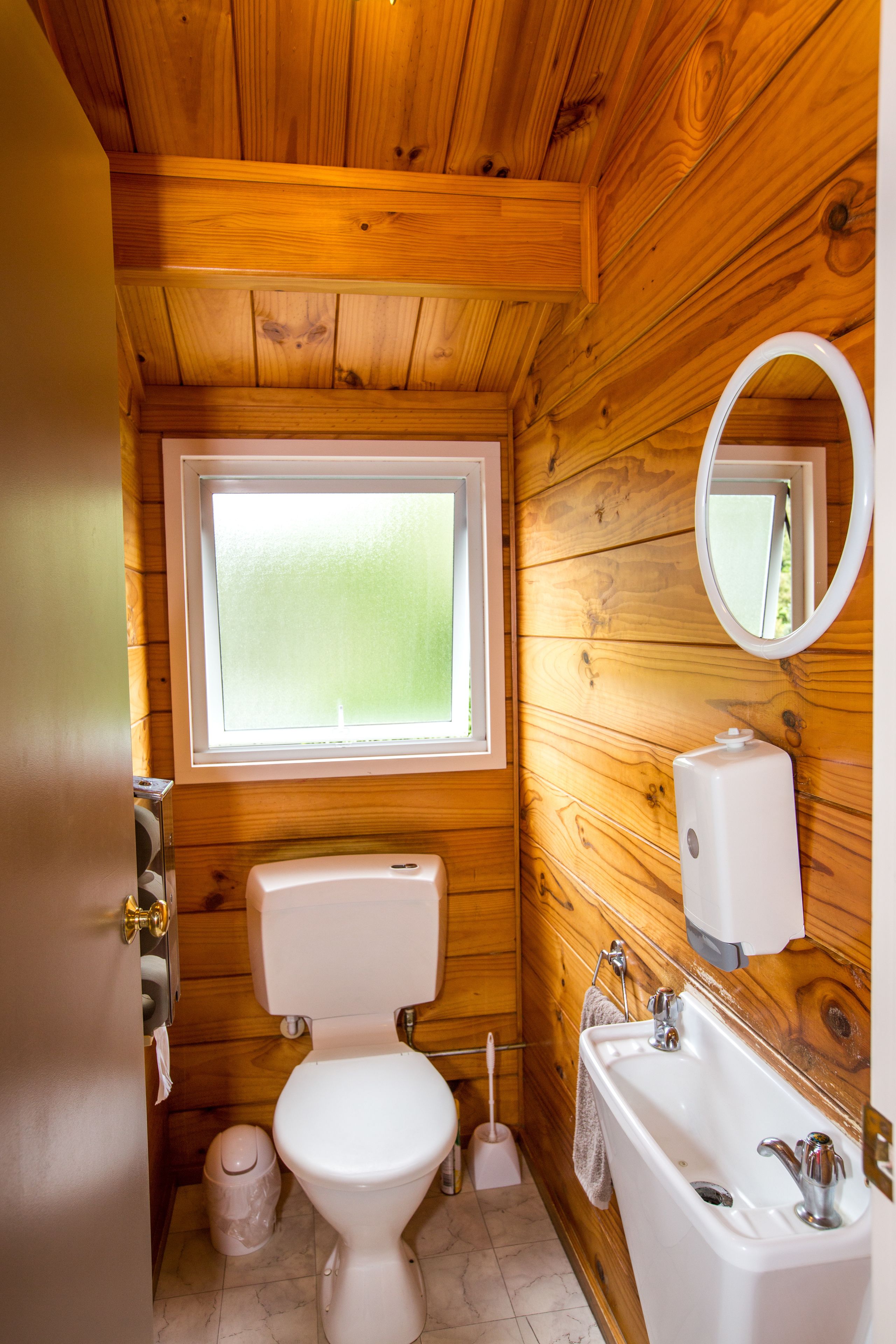 Un baño de cabaña de madera, compacto, con inodoro, lavamanos y ventana.
