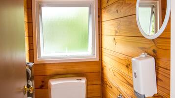 Un baño de cabaña de madera, compacto, con inodoro, lavamanos y ventana.