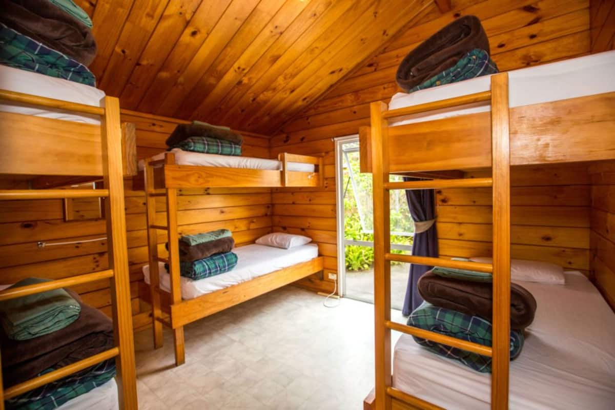 Una cabaña con tres literas, paredes de madera y una ventana.