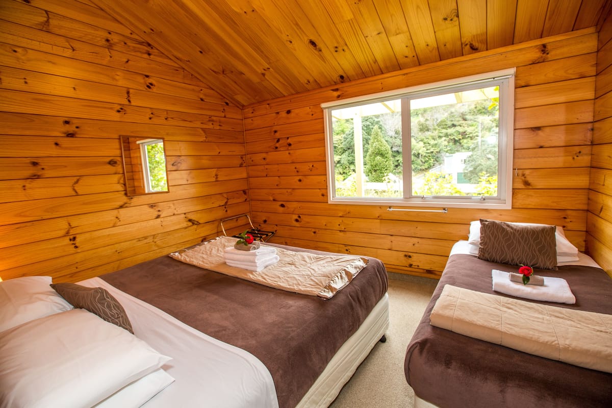Una habitación tipo cabaña de madera con dos camas, una ventana y un ventanal pequeño sobre la cama izquierda.