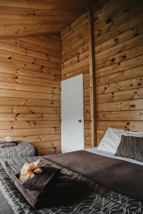 Una habitación de cabaña de madera con una cama, una mesita de noche y una puerta.