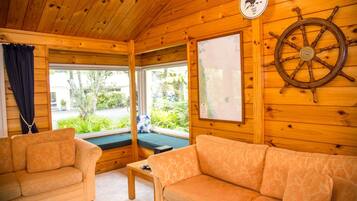Een gezellig chalet binnen met houten wanden, een houten plafond, twee banken, een kleine tafel en een groot raam met uitzicht op groen.