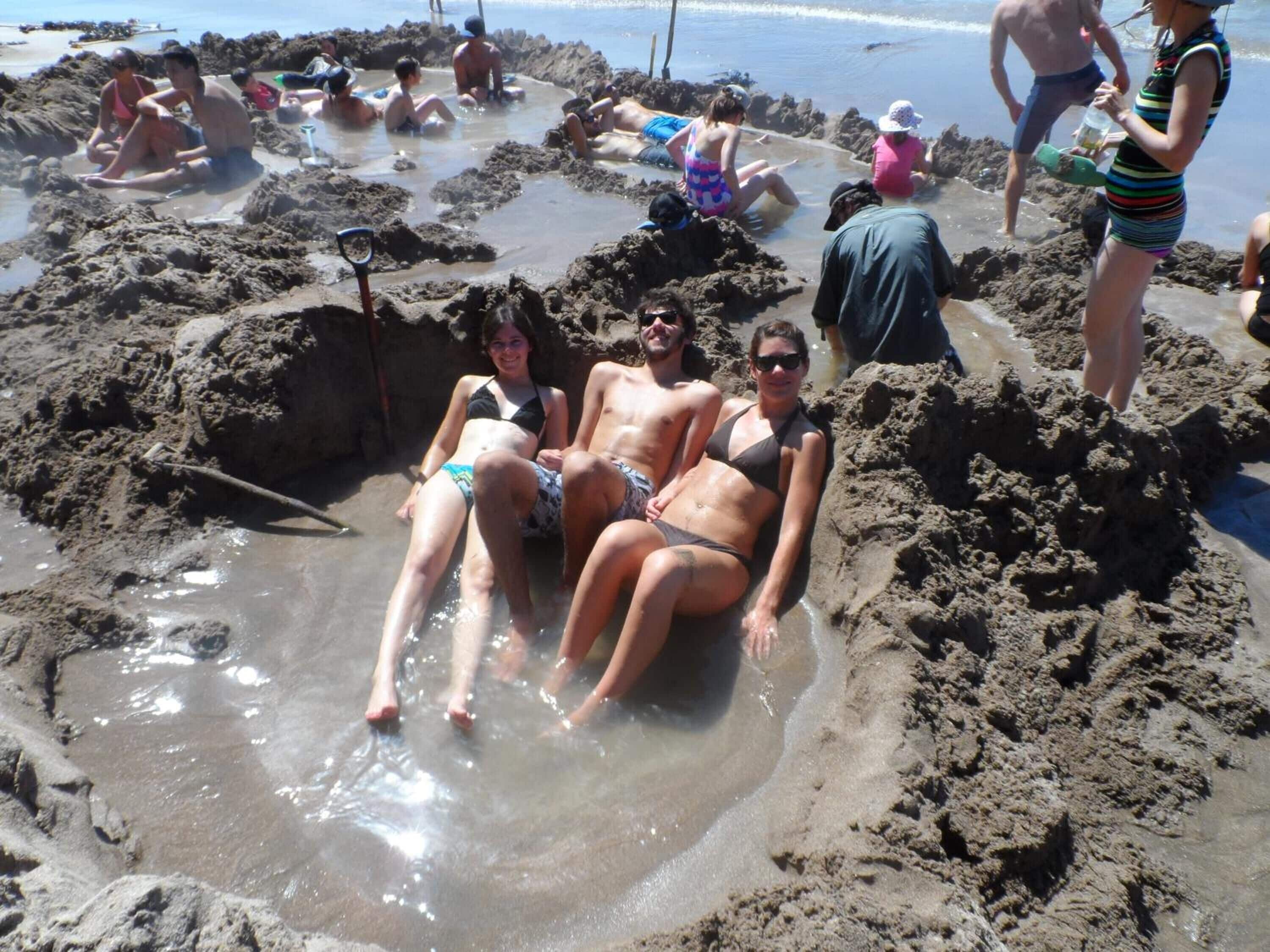 A sandy beach with people sitting and standing in the water.