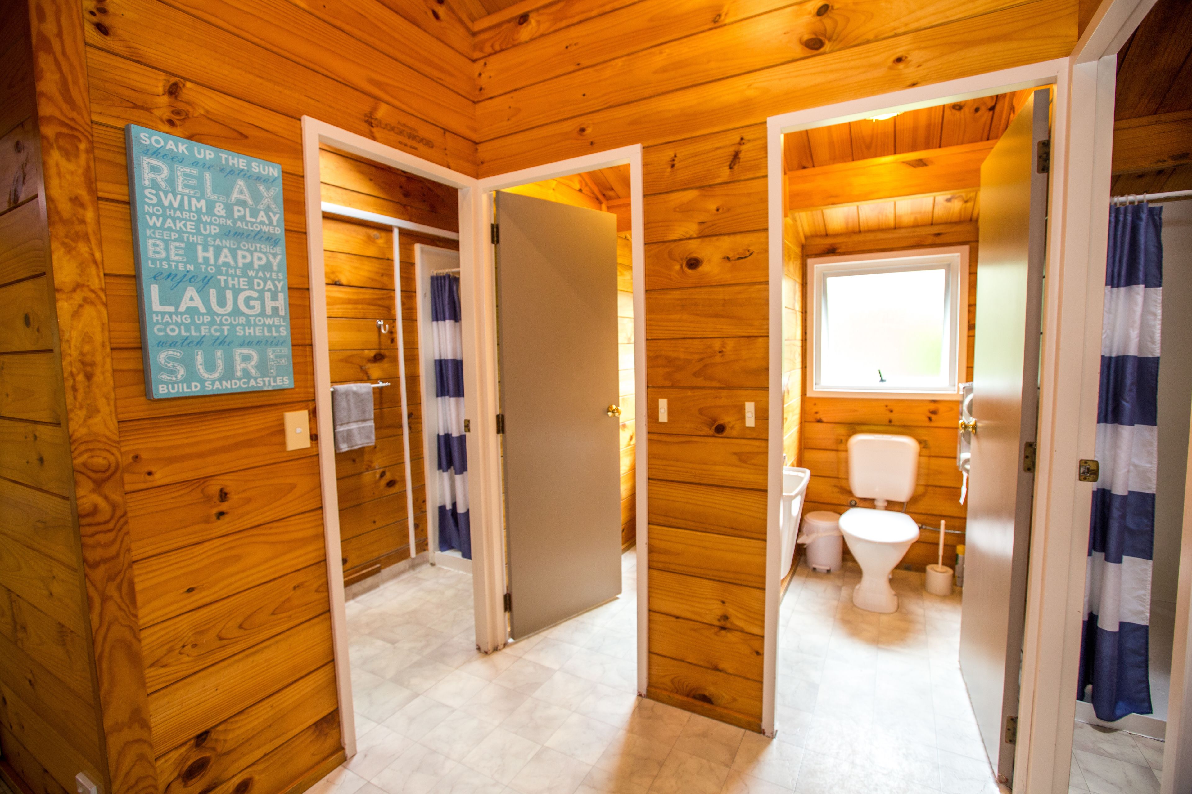 Interno di una baita in legno con bagno, che include un WC, una finestra e un cartello con frasi motivazionali.