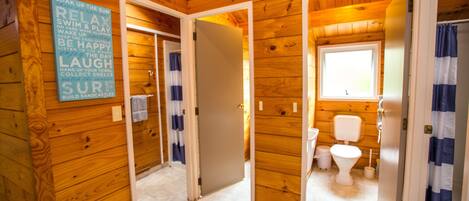 Interno di una baita in legno con bagno, che include un WC, una finestra e un cartello con frasi motivazionali.