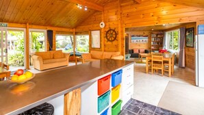 Interior de una cabaña de madera con cocina, mesa de comedor y un ventanal grande.