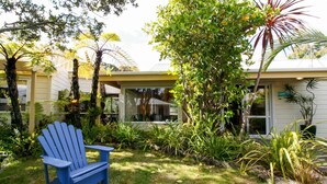 Una casa con jardín delantero, una silla Adirondack azul y diversas plantas.