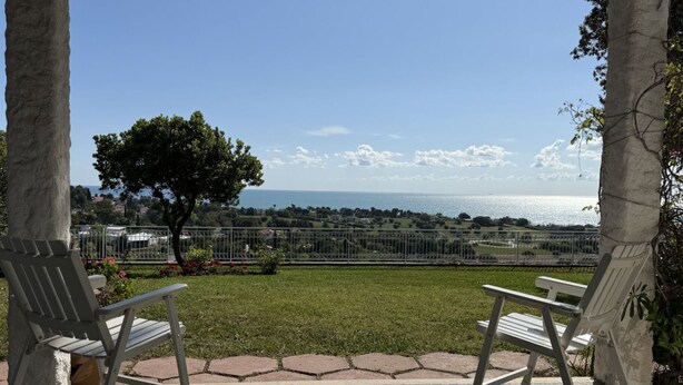 Un patio con dos sillas blancas, piso estampado y vista al mar y paisaje lejano.
