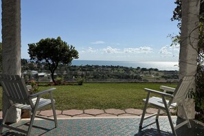 A patio with two white chairs, a patterned floor, and a view of the sea and distant landscape.