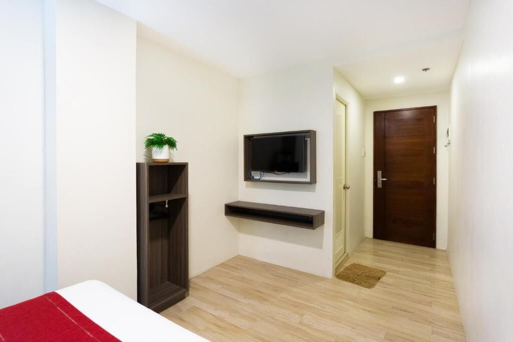 A room with a bed, a TV mounted on the wall, a wooden door, and a small plant on a shelf.