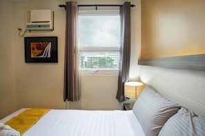 A hotel room with a bed, a window with curtains, a wall-mounted air conditioner, and a framed picture. - The Rooms by Alinace at Mango (Cebu City)