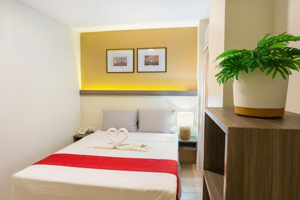 Habitación de hotel con una cama, una mesita de noche con lámpara, teléfono y un cuadro colgado en la pared.