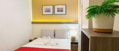 Habitación de hotel con una cama, una mesita de noche con lámpara, teléfono y un cuadro colgado en la pared.