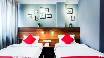 A hotel room with two beds, a wooden headboard, a nightstand with a phone, and framed pictures on the wall.