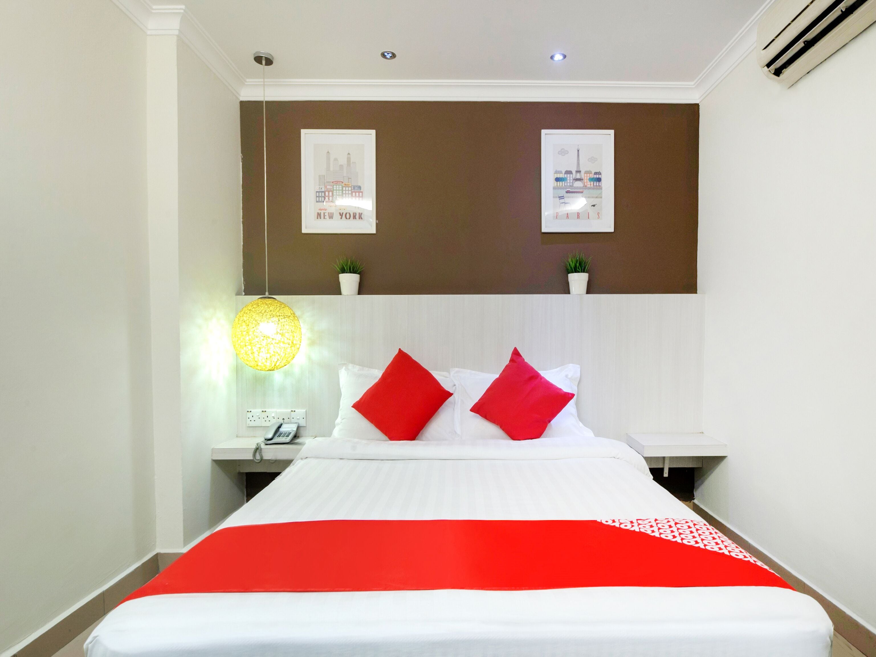 Una habitación de hotel con una cama, una mesita de noche, una lámpara y dos cuadros colgados en la pared.