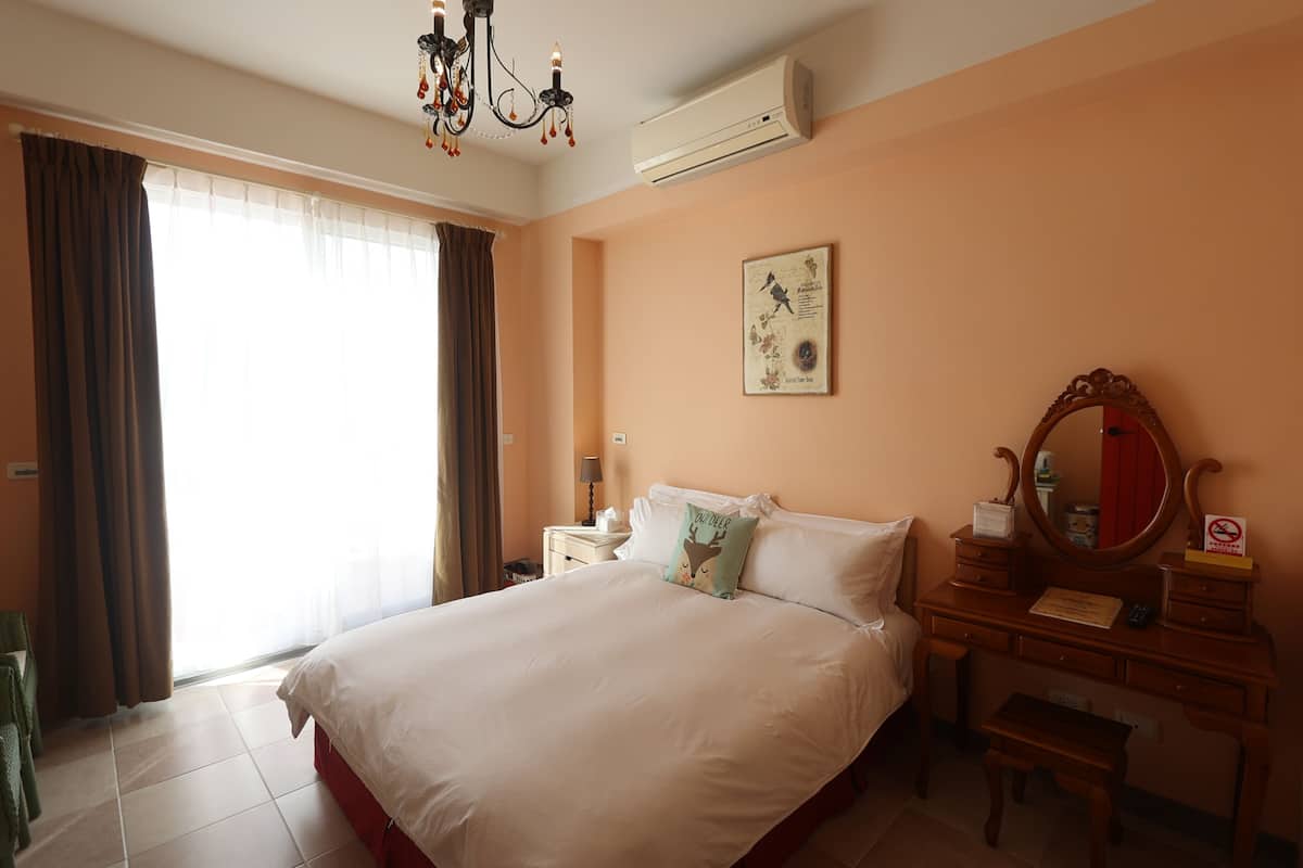 Quarto de hotel com uma cama grande, penteadeira com espelho, mesa de cabeceira e janela com cortinas.