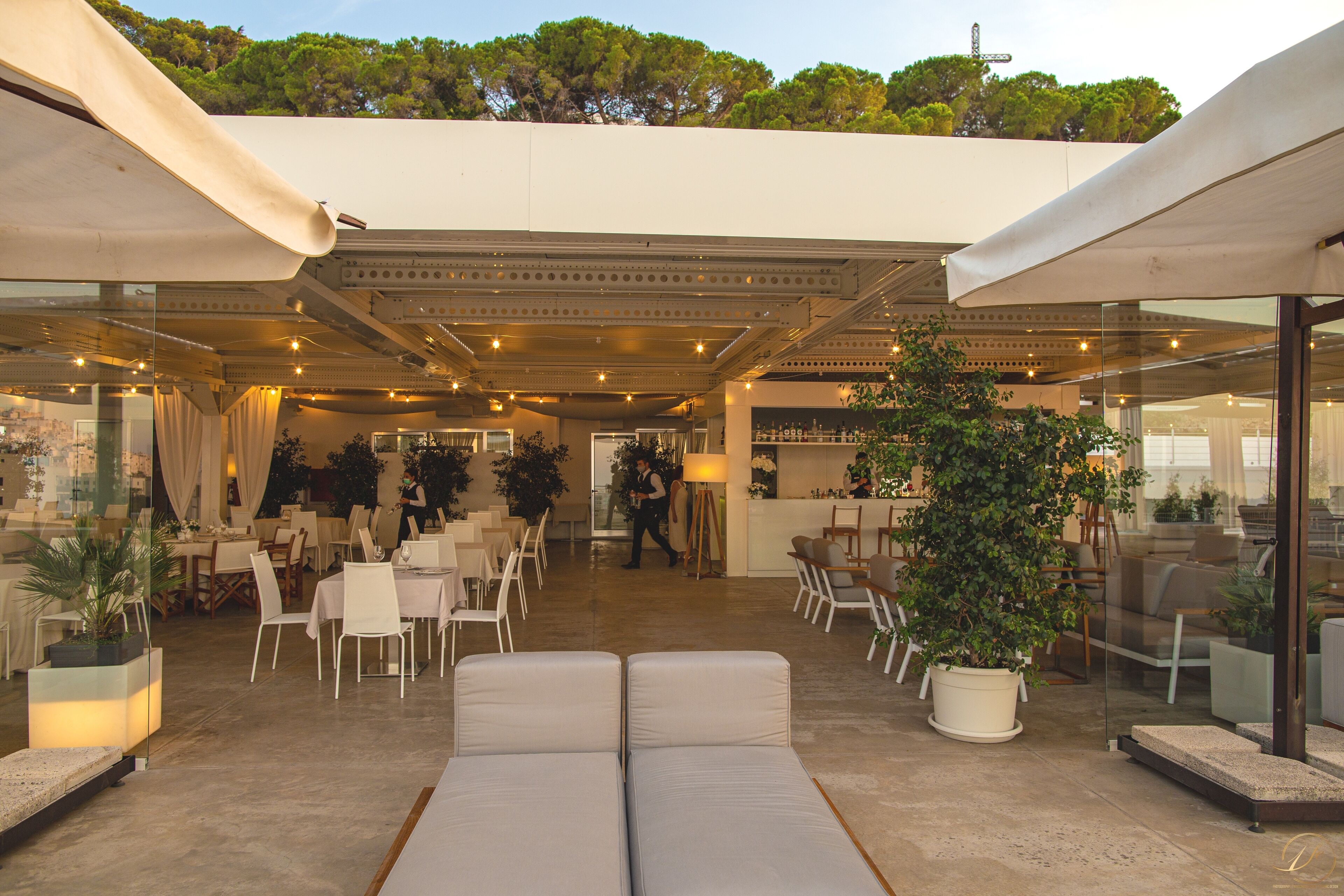 Un espace extérieur aménagé avec des tables et des chaises, un comptoir d’accueil et des plantes en pot.