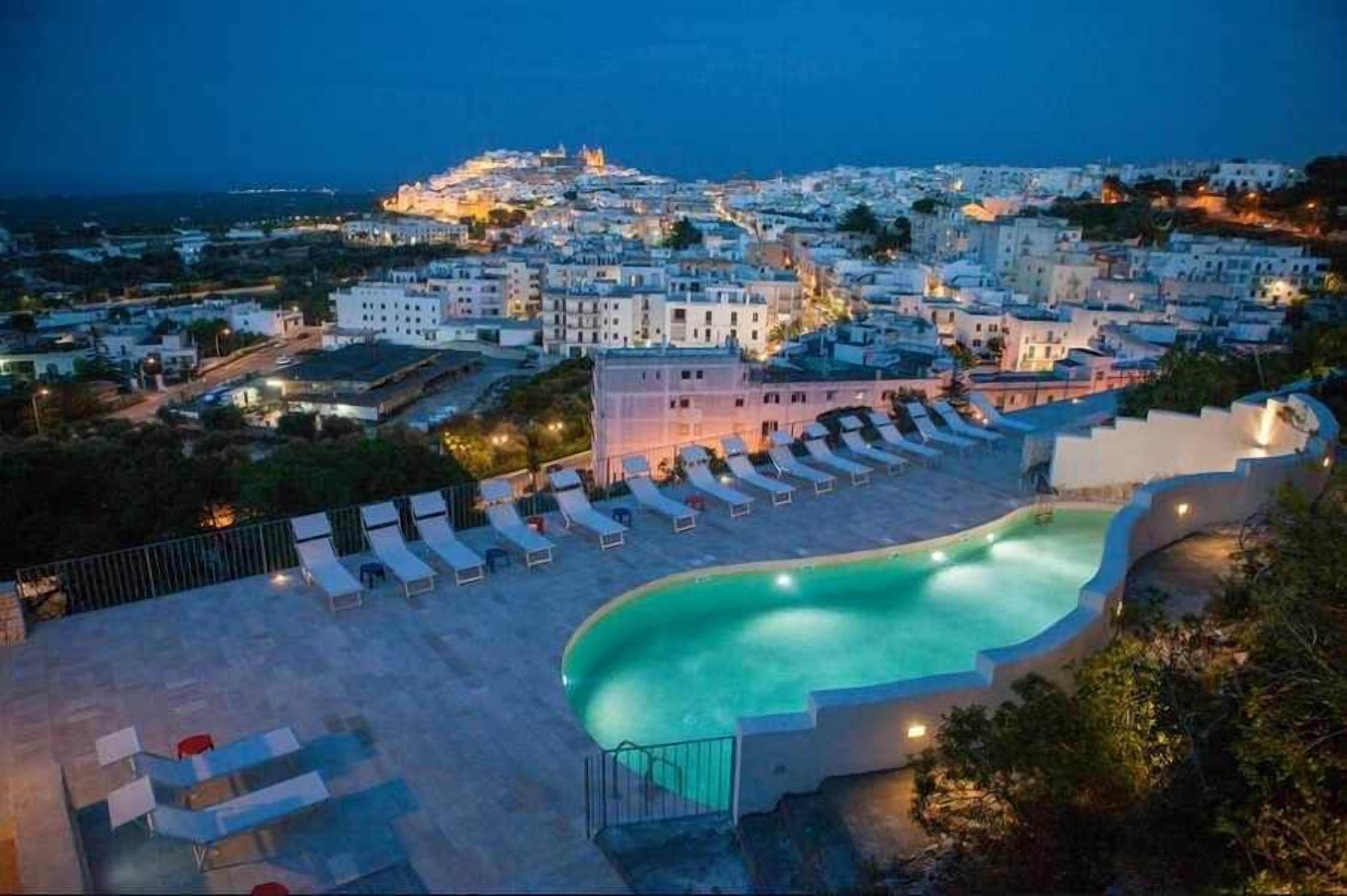 A pool area with lounge chairs and a view of a coastal town at dusk.