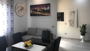 A modern living room with a sofa, a dining table with fruit, a world map clock, and cityscape artwork. - Cris&Giuli House (Barberino Tavarnelle)