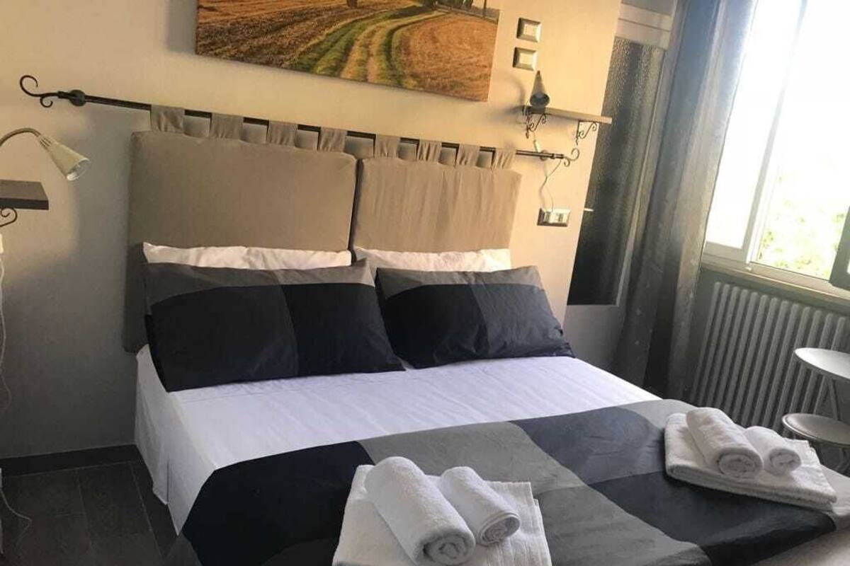 A neatly made bed with a checkered bedspread, two rolled towels, and a headboard with curtains.