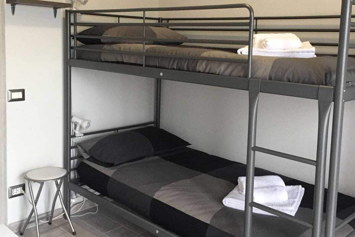 A bunk bed room with a painting of a landscape on the wall, a small table, and a chair.