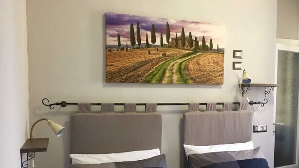 A bedroom with two beds, a headboard, a bedside lamp, and a wall-mounted painting of a landscape. - Cris&Giuli House (Barberino Tavarnelle)