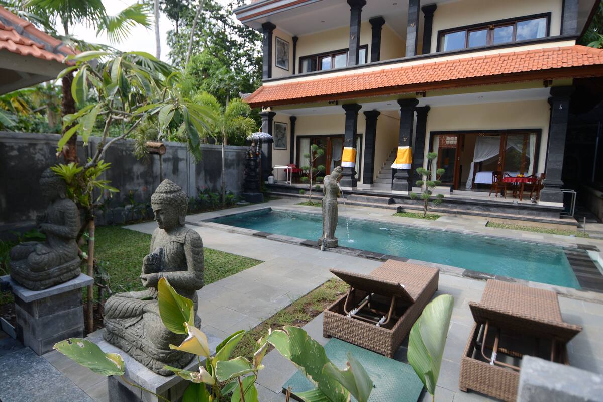 A serene pool area with a statue, outdoor furniture, and a building with a tiled roof.