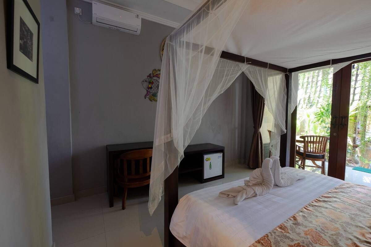 A bedroom with a bed, a bedside table, a chair, and a window with a view of greenery.