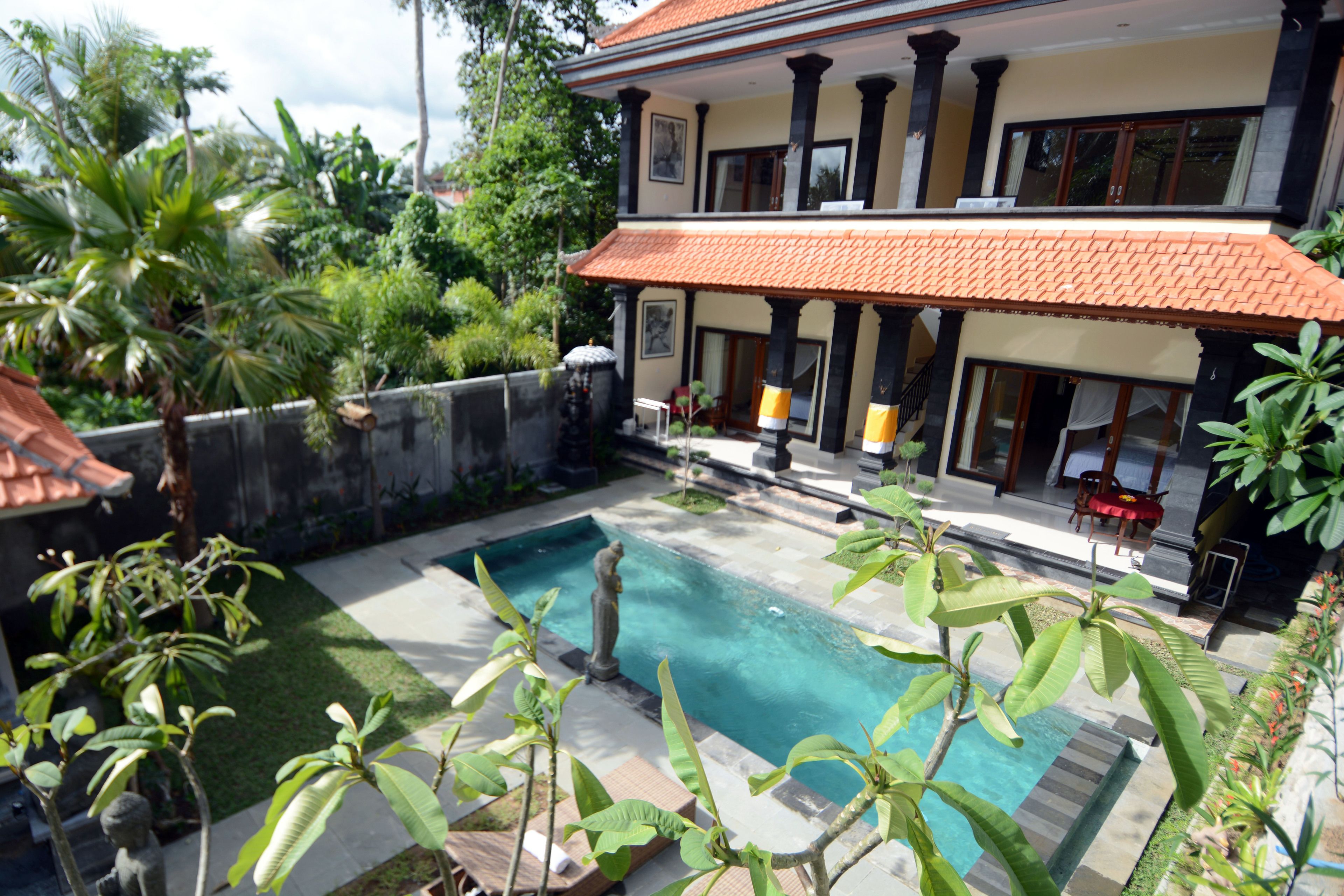 A two-story house with a swimming pool, surrounded by lush greenery and a tiled roof.