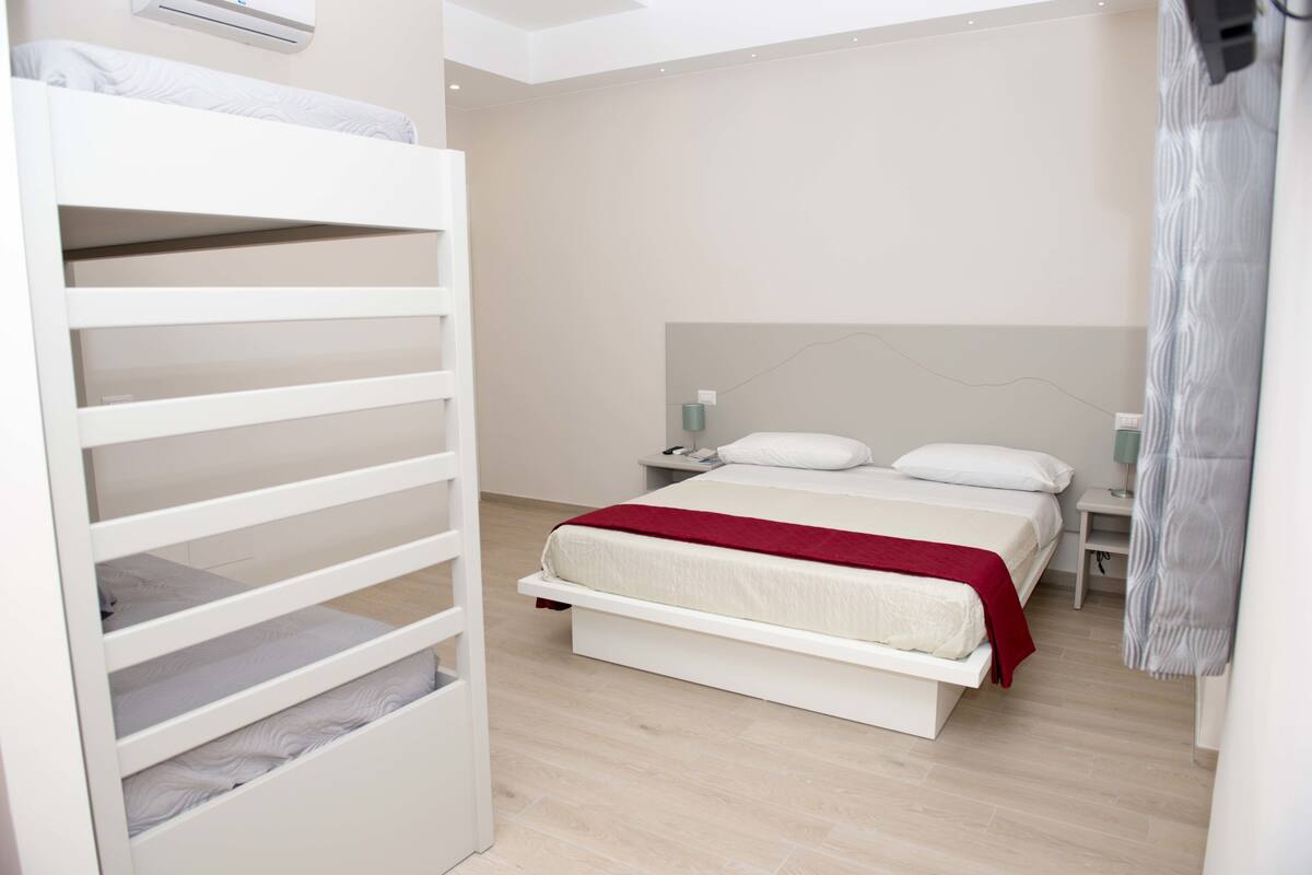 Een moderne slaapkamer met een stapelbed, een eenpersoonsbed, een nachtkastje en een bedtafel.