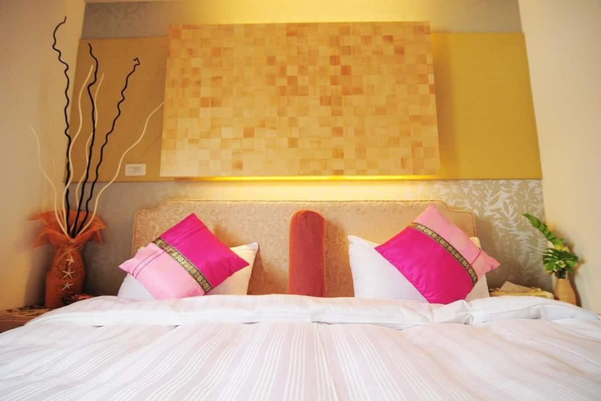 A hotel room with a bed, pillows, a wall art piece, and a vase with branches.