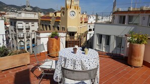 Eine Terrasse mit Tisch und Stühlen, Blumentöpfen und einem Uhrturm im Hintergrund.