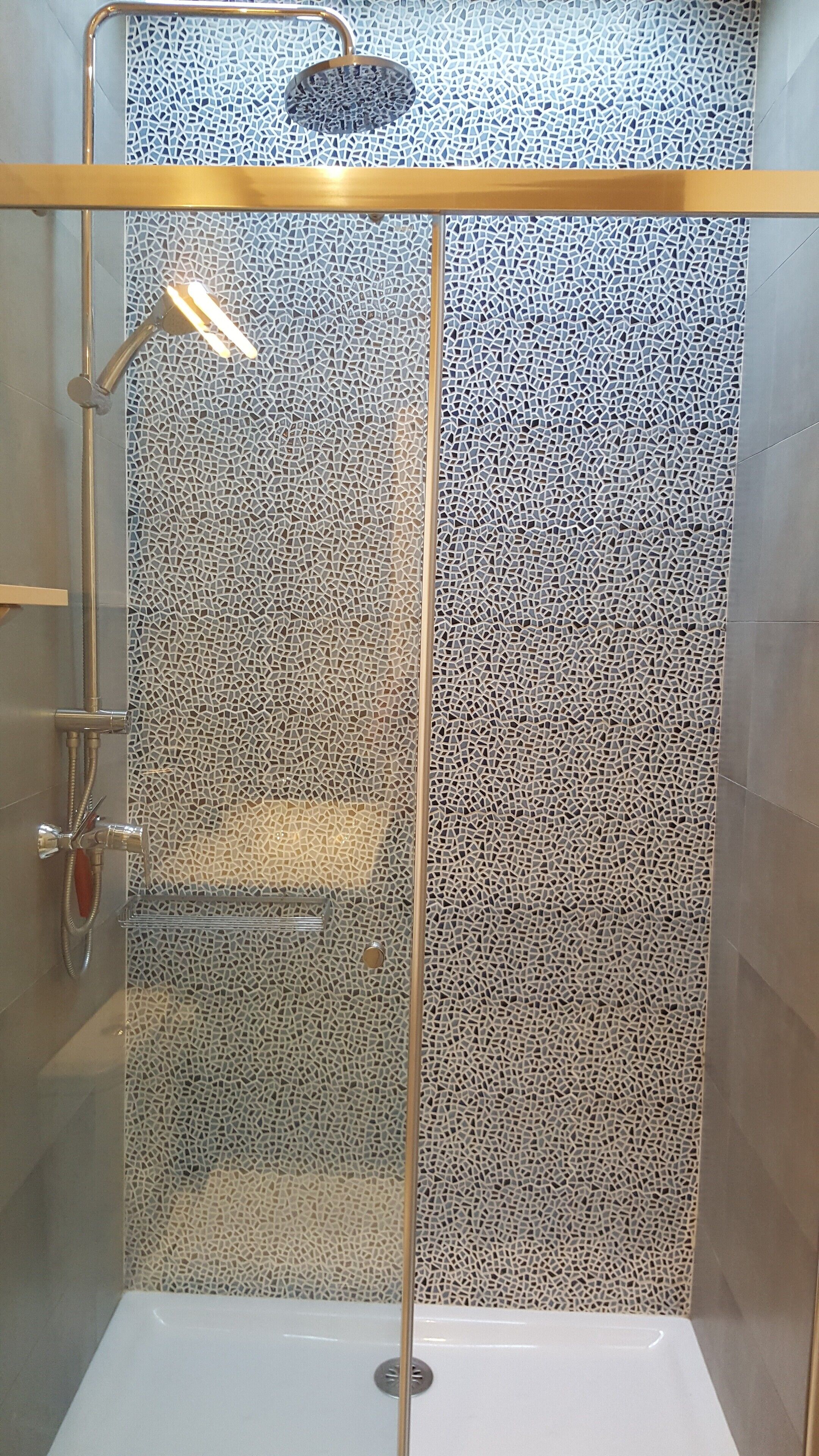Un espace de douche doté d’un mur recouvert de mosaïques, d’une porte en verre et d’un pommeau de douche à main.