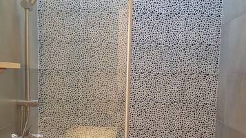 Un espace de douche doté d’un mur recouvert de mosaïques, d’une porte en verre et d’un pommeau de douche à main.