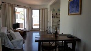 A spacious living room with a sofa, a TV, a dining table with chairs, a bookshelf, and a view through a glass door. - The Sky penthouse in the center of town with panoramic views and sunny terrace (Sitges)