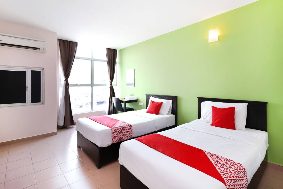 A hotel room with two beds, a window with curtains, a desk, and a green wall.